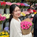 Cô gái xinh đẹp bên hoa tulip trong không gian chợ hoa đầy màu sắc